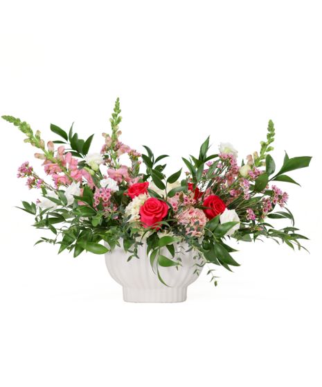 A wide garden style floral arrangement in a white ceramic container featuring hot pink roses, soft white flowers, and lush green foliage in a natural, flowing shape.