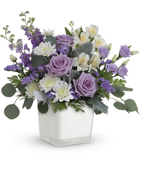 A mix of lavender roses, larkspur, white mums, statice and dusty miller foliage, designed in a white container.
