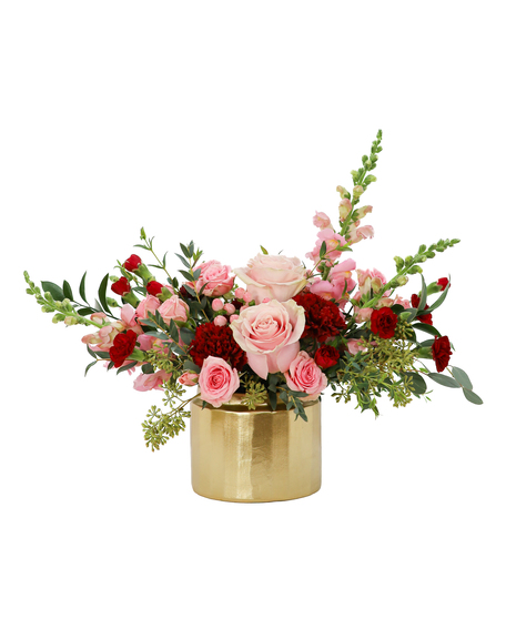 A romantic mix of pink roses, red blooms, and soft greenery arranged in a brushed gold pot, featuring varied heights and a lush, garden-inspired shape.