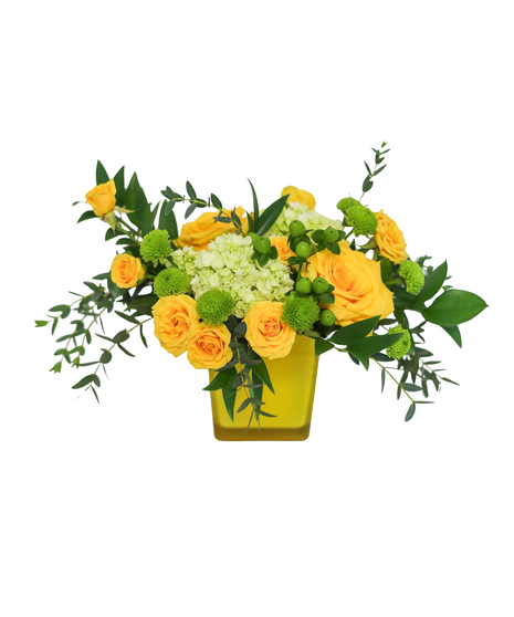Yellow roses, green hydrangea, green button mums, berries, and eucalyptus arranged in a yellow glass cube vase.