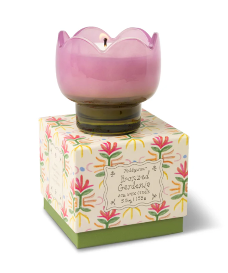 A purple glass tulip shaped candle on top of a floral patterned box.