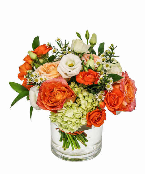 Orange roses and spray roses, white lisianthus, green hydrangea, and white asters arranged in a clear glass cylinder vase.