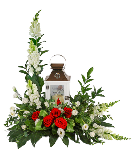 Sympathy floral arrangement with tall white snapdragons, red roses, and white flowers surrounding a white memorial lantern with a red cardinal, set in lush greenery.