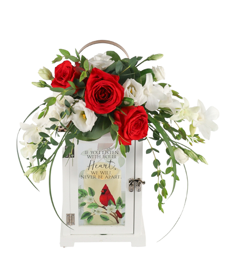Sympathy floral display with red roses and white orchids atop a white memorial lantern, with trailing greenery and buds.