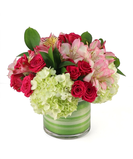 Vivid pink roses and pink alstroemeria mixed with green hydrangea and green foliage arranged in a clear glass vase with a green leaf-wrapped interior