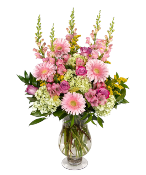 Pink and yellow floral arrangement with roses, gerbera daisies, snapdragons, hydrangeas, and greenery in a clear glass vase.